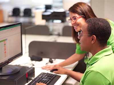 One employee helps another while they look at a computer.